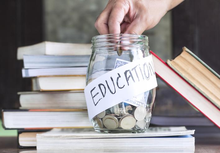 hand putting coins in a jar labelled education, surrounded by books